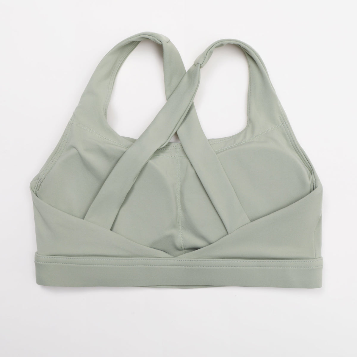 A sage green sports bra with a unique crisscross crossover front strap design, laid flat on a clean white background.